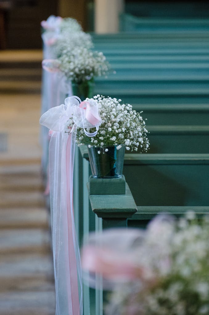 Elegant white and pink floral decorations on church pews create a romantic wedding atmosphere.