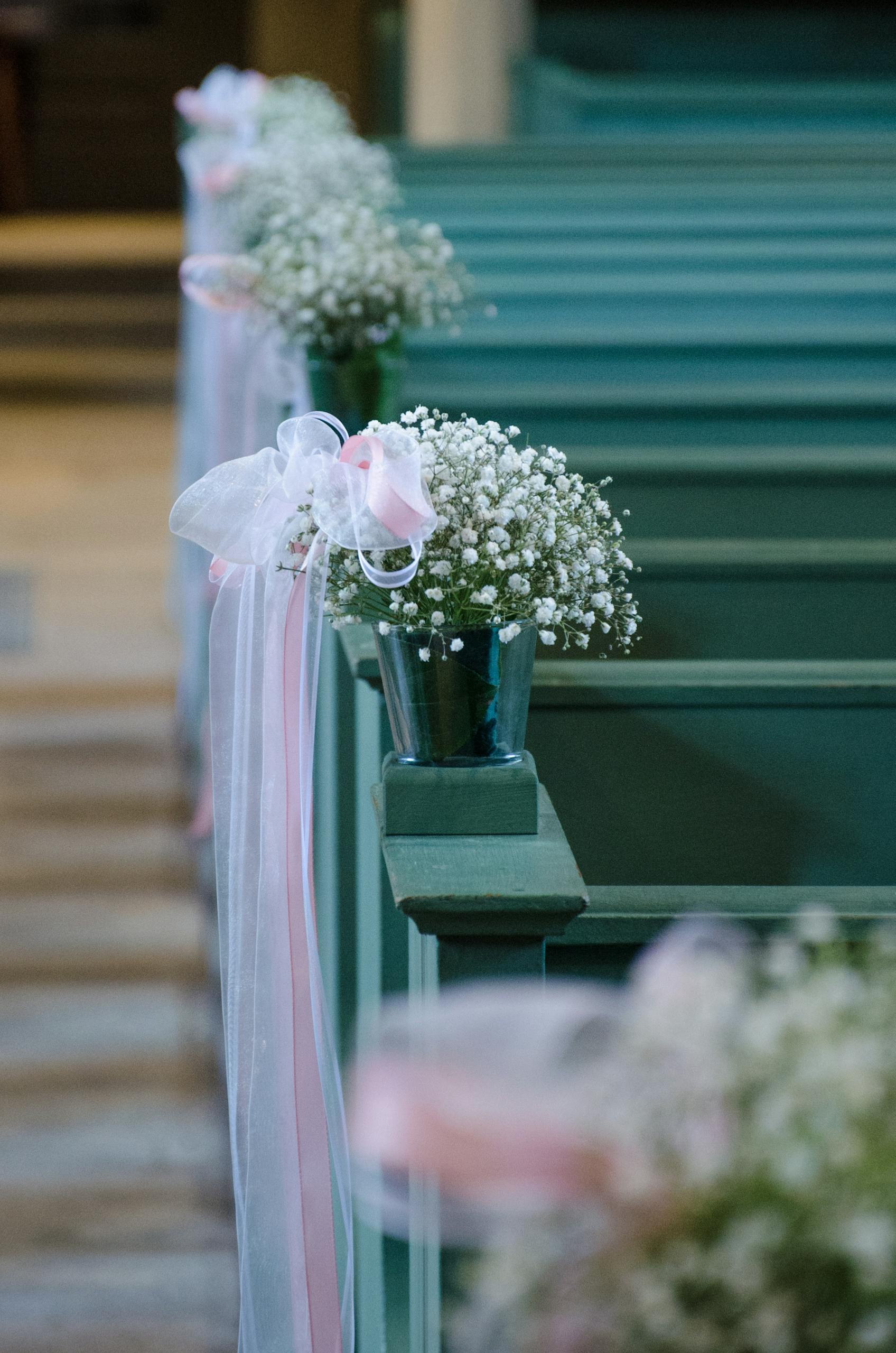 Elegant white and pink floral decorations on church pews create a romantic wedding atmosphere.