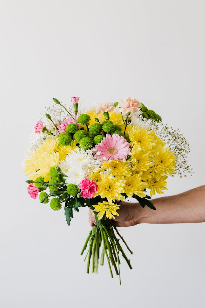 Vibrant bouquet with yellow, pink, and white flowers held against a white backdrop.
